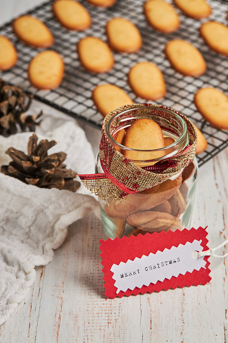 From above of tasty Christmas biscuits placed on metal baking net and glass jar on table with assorted wrapping supplies