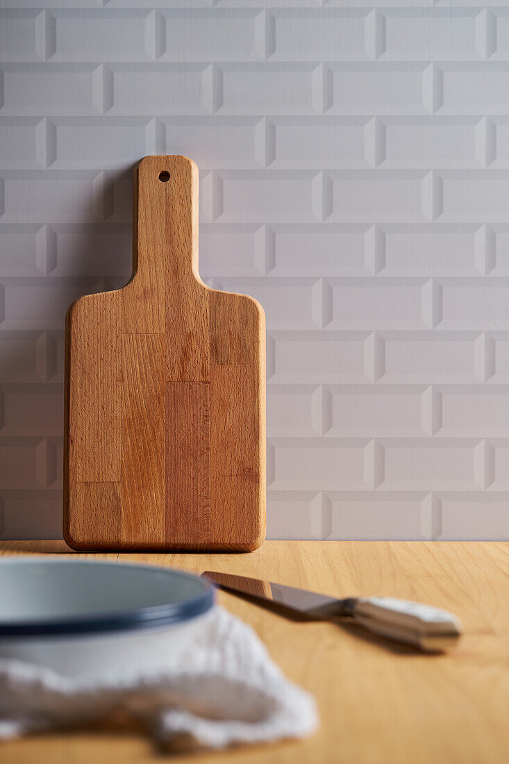 Holzschneidebrett in Wandnähe auf Tisch mit Schüssel und Messer in heller Küche