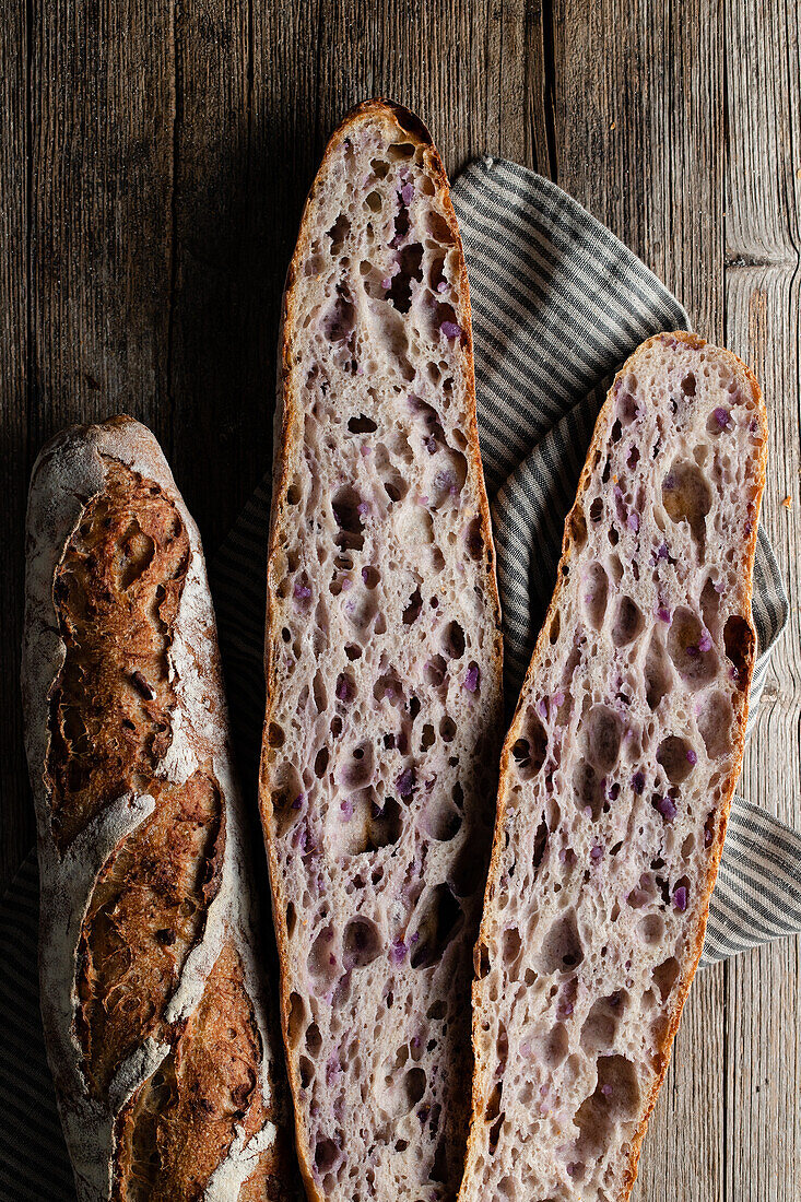 Top view of cut and whole sourdough baguettes with crunchy crust placed on wooden table