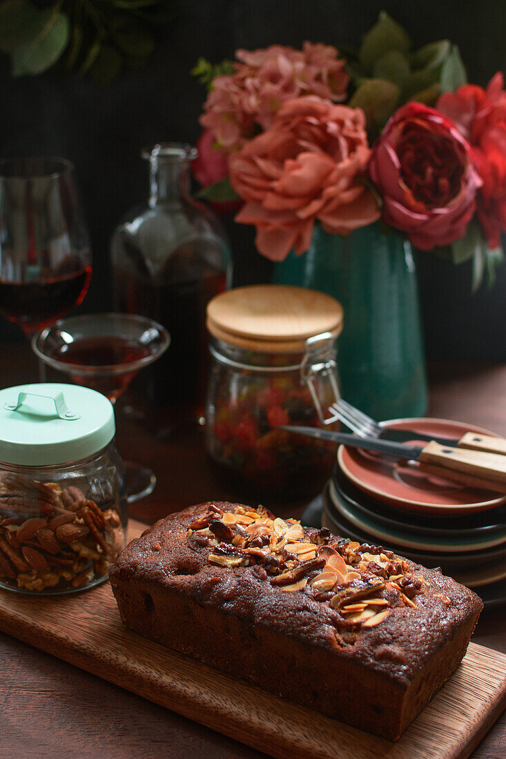 Tasty baked pound cake topped with almond flakes served on wooden cutting board on table with alcohol drink and berries