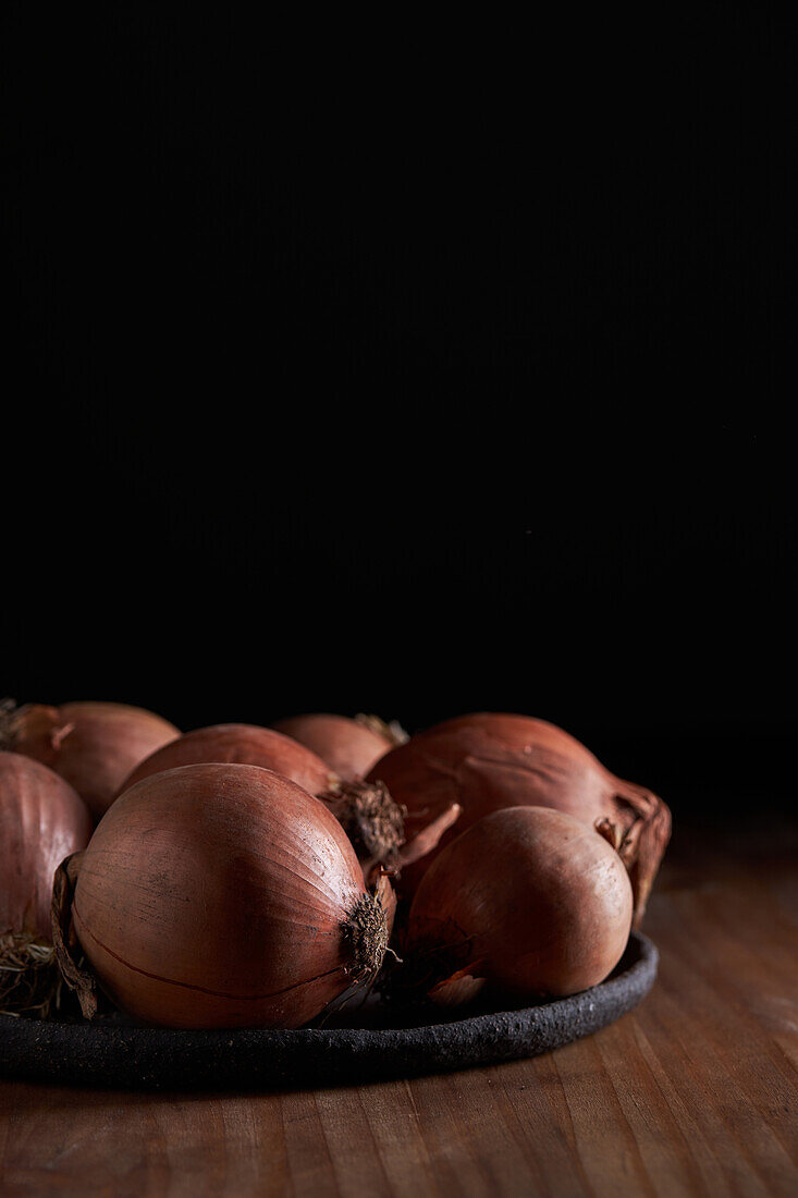 Strauß frischer ungeschälter Zwiebeln auf Teller auf Holztisch gelegt