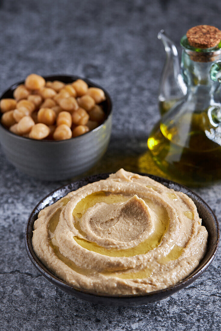 From above bowls of fresh hummus and chickpeas placed on gray marble table near oil in kitchen