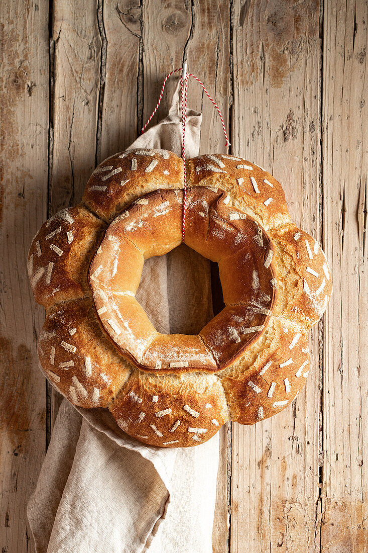 Decorative round baked loaf of bread with white patterns hanging on wooden wall with towel in light kitchen at home