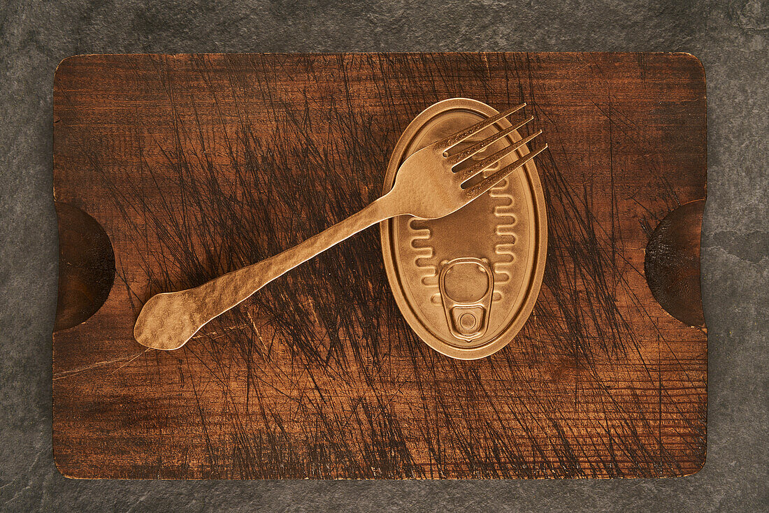 From above scratched chopping board with fork and sealed can with preserved food on rustic lumber table