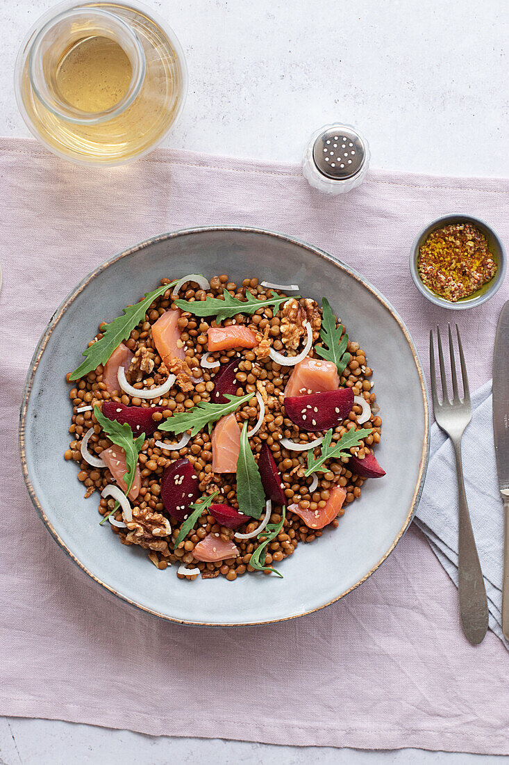 Nahaufnahme eines Lachs- und Linsensalats von oben auf einem Tisch mit rosa Tischtuch