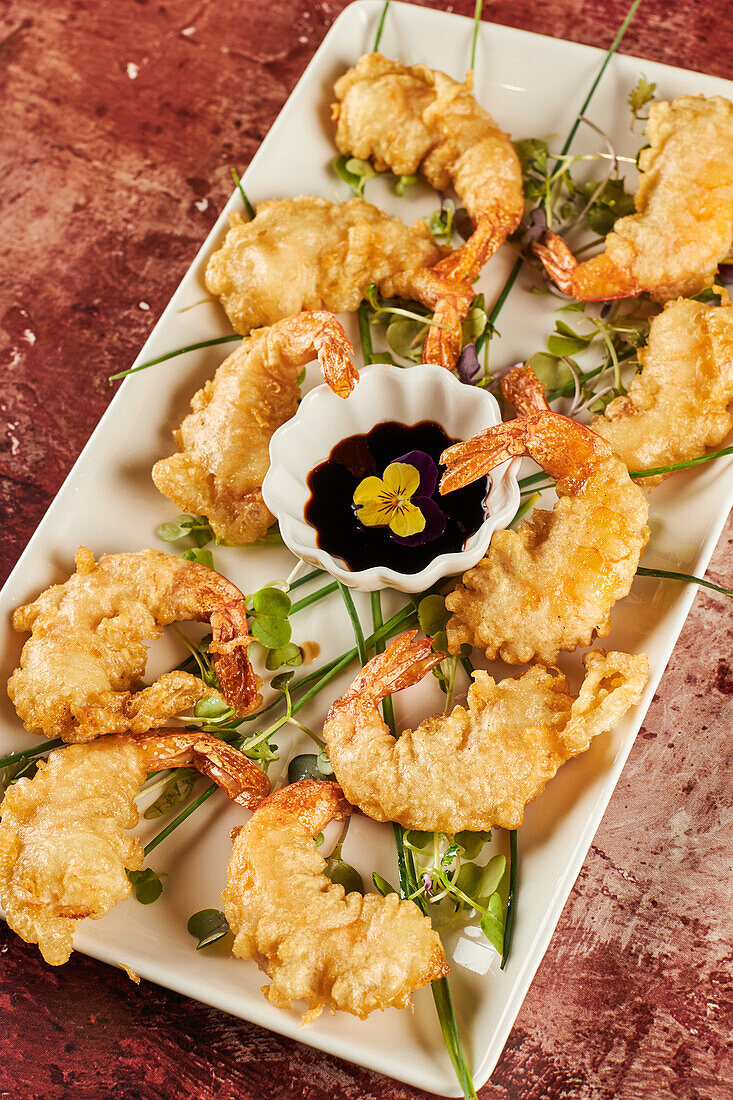 From above tasty shrimp tempura with greens and soy sauce served on plate on restaurant table