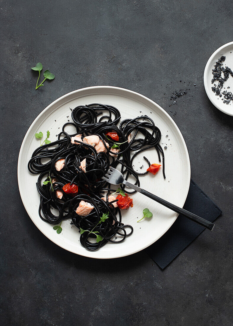 From above black ink spaghetti with salmon in ceramic plate on dark background