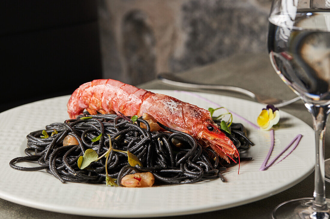 Black spaghetti with squid ink garnished with prawns and sprouts and served on plate during lunch in restaurant