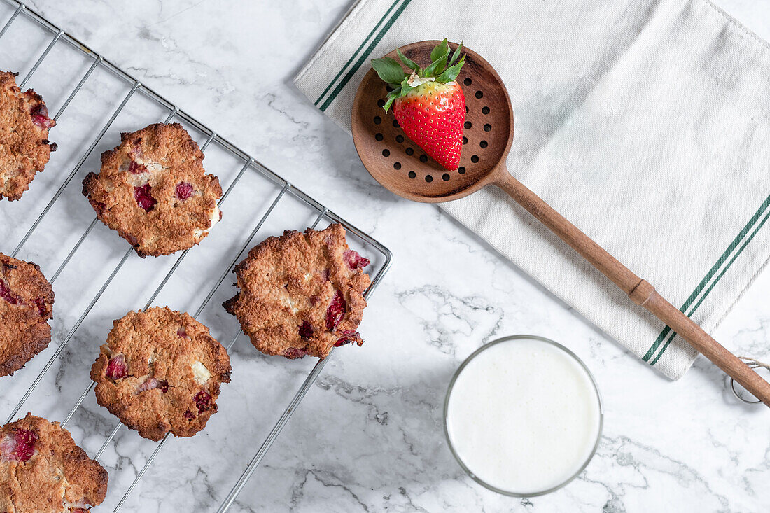 Top view of tasty homemade cookies with strawberries placed on table with glass of fresh milk