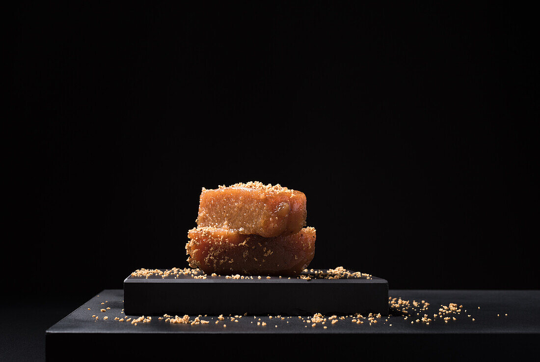 Gourmet quince jelly paste in ceramic plate sprinkled with sesame seeds on black background