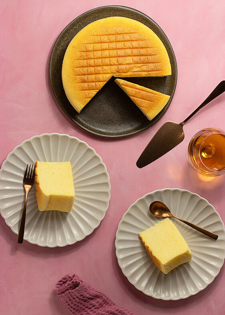 Top view of delicious cotton cheesecake served on plates near glass and spatula on pink background