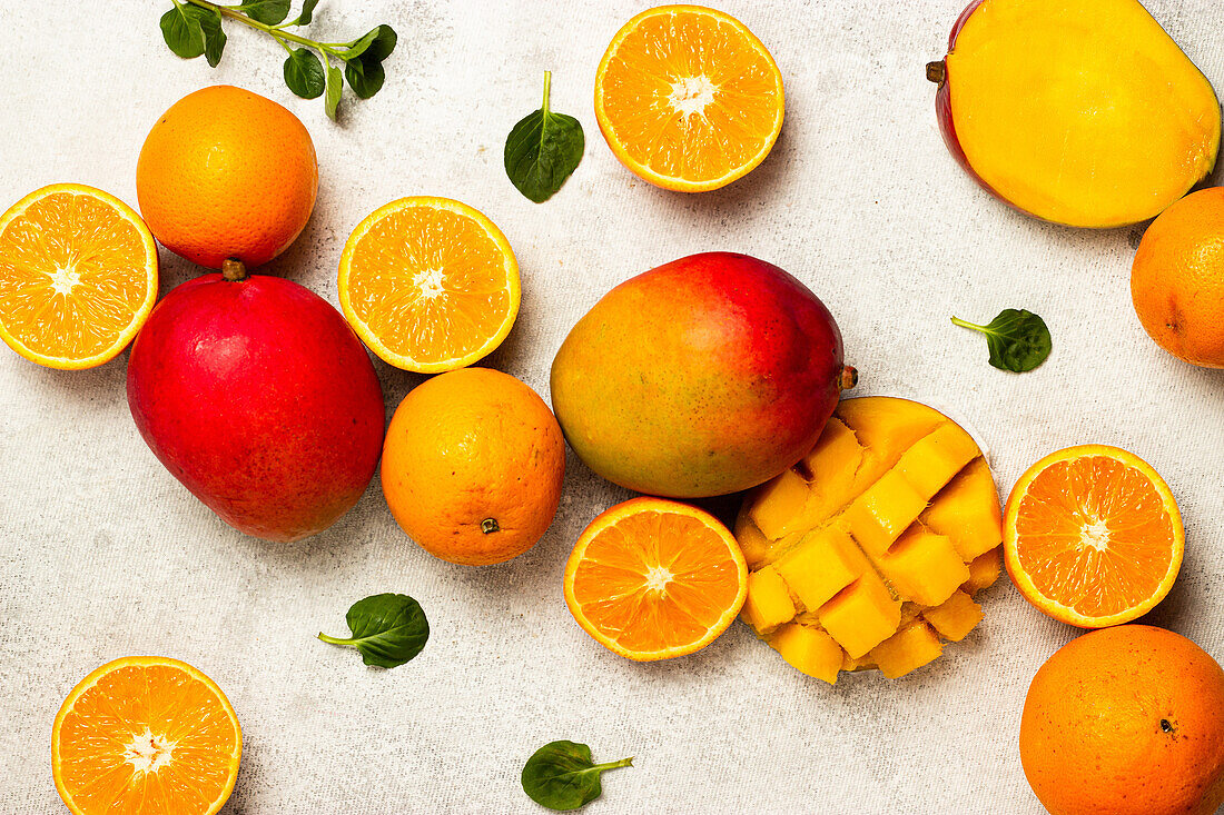 Top view of ripe juicy oranges and mangoes placed near green leaves on gray surface