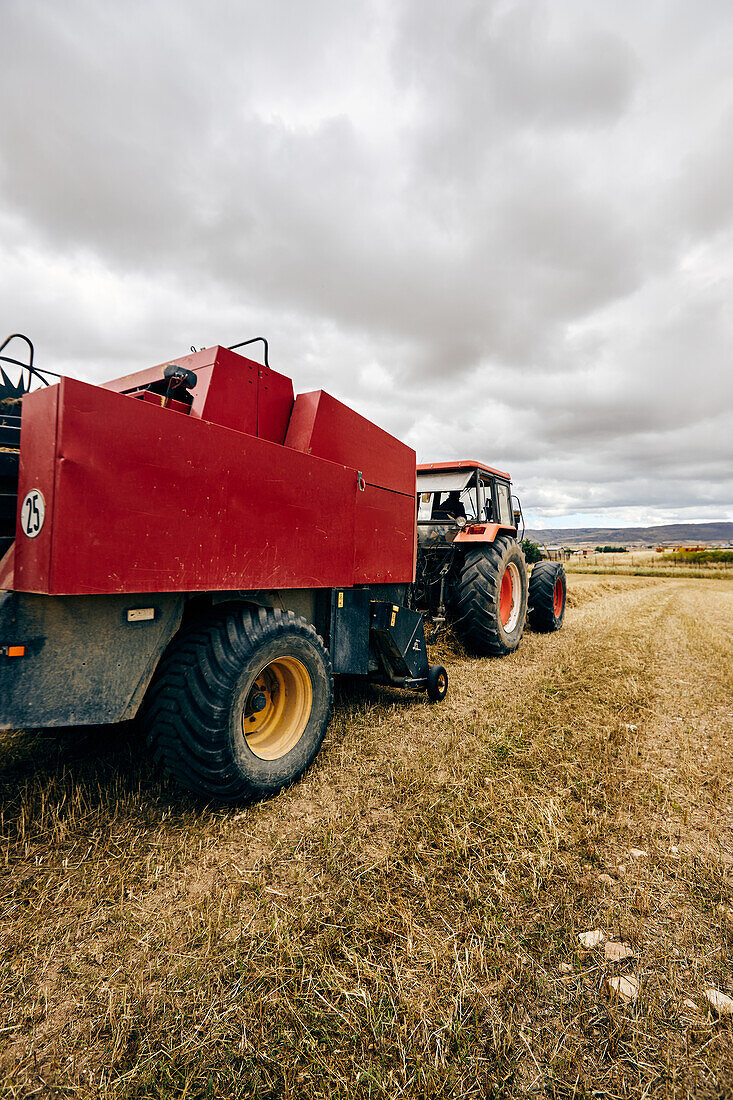 Dried hay roll and modern tractor placed on agricultural field in mountainous area in summer