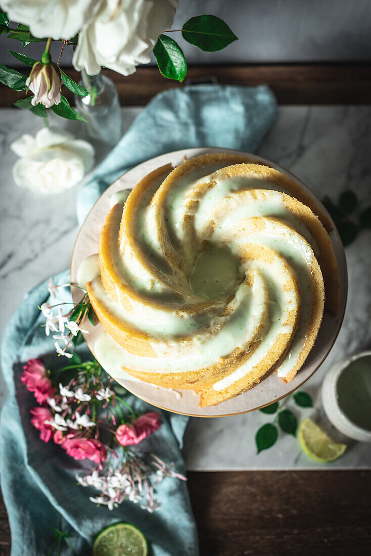 Top view of tasty lime sponge cake served on white plate near flowers and lime slices