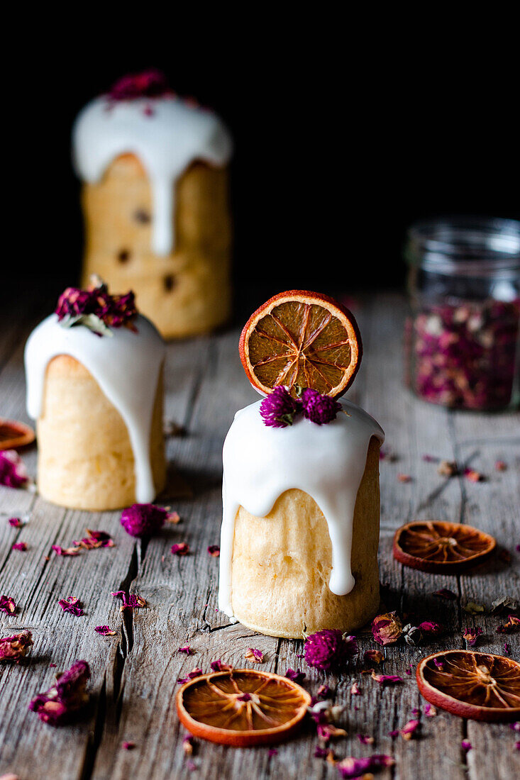 Several delicious homemade kulichs poured with sweet glaze and decorated with pieces of dry orange and flowers on wooden table