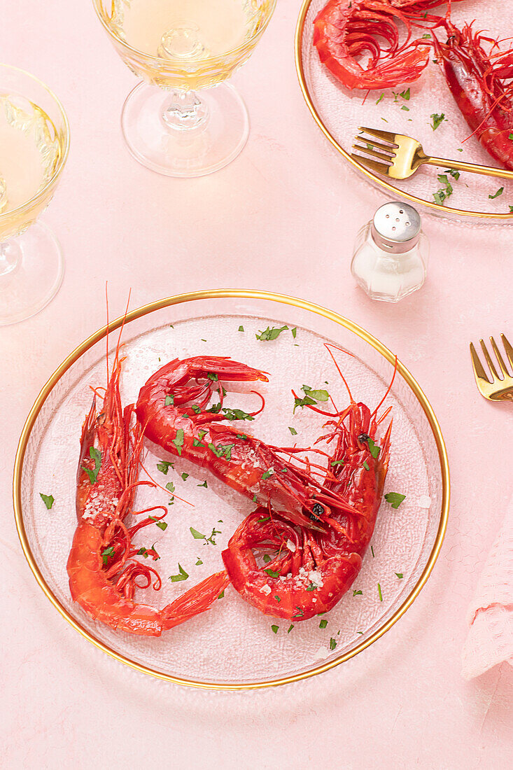 From above glass plate with tasty fried tiger shrimps placed near glass of wine on table pink background