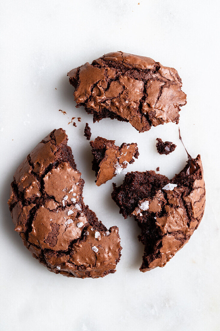 Draufsicht auf einen hausgemachten gebrochenen süßen Schokoladen-Brownie-Keks mit Rissen und Krümeln auf weißem Hintergrund in einer hellen Küche