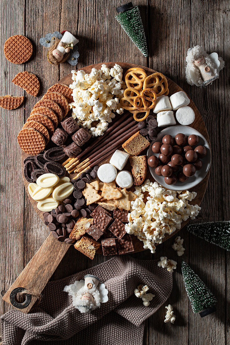 Top view of various chocolates with cookies and popcorn arranged on wooden table with christmas figures