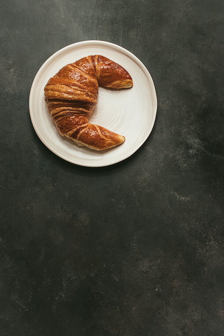 Top view composition with appetizing freshly baked crusty croissant served on white and black plate on table