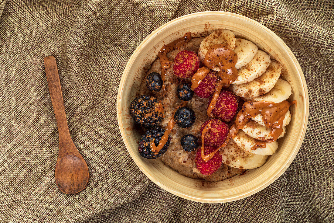 Overhead view of bowl with mix of ripe berries and banana slices covered with delicious caramel sauce on crumpled sackcloth