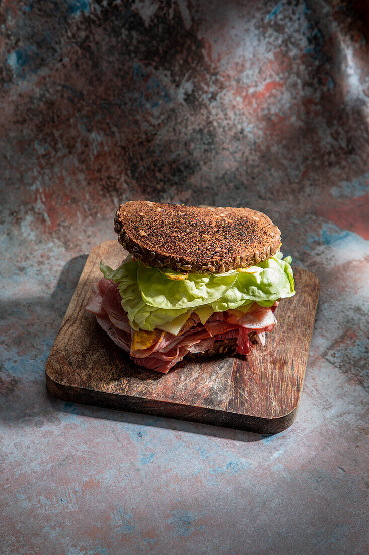 High angle of appetizing sandwich with fresh crusty bread above lettuce leaves and bacon on wooden board