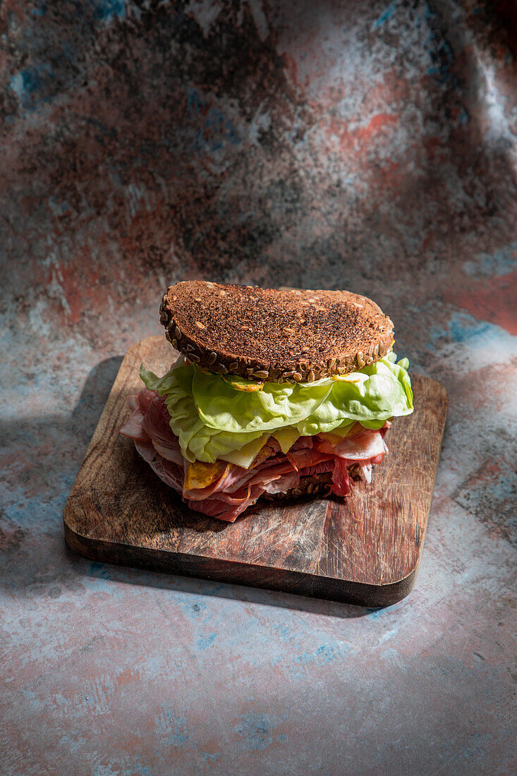 Hoher Blickwinkel auf ein appetitliches Sandwich mit frischem, knusprigem Brot über Salatblättern und Speck auf einem Holzbrett