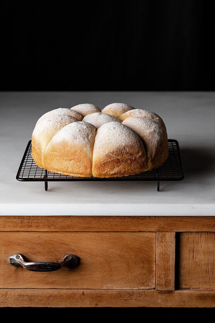 Appetizing soft bread buns on baking tray placed on wooden counter near black wall