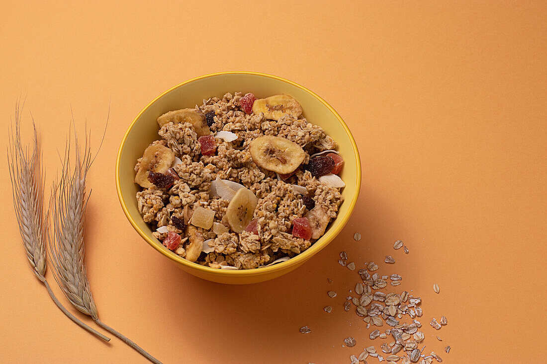 From above crispy granola with dried fruits in bowl on light table brown background