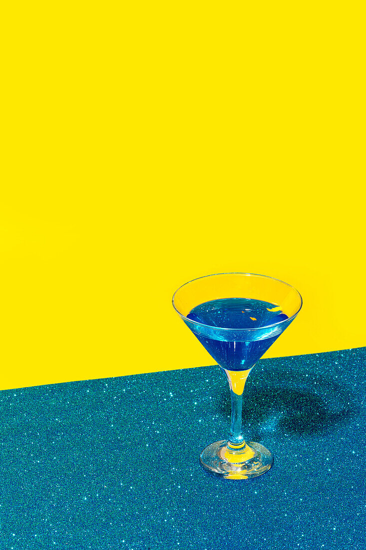From above of creative cocktail in glass crystal martini glass placed against bright blue and yellow background