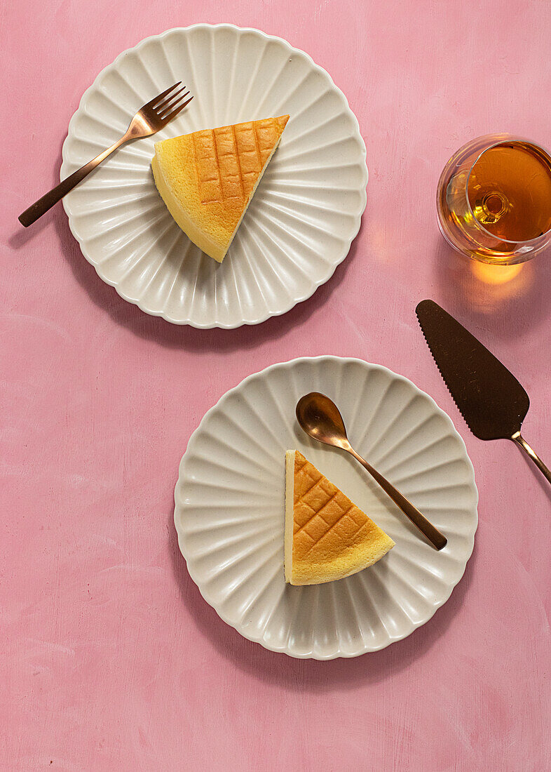 Top view of delicious cotton cheesecake served on plates near glass and spatula on pink background