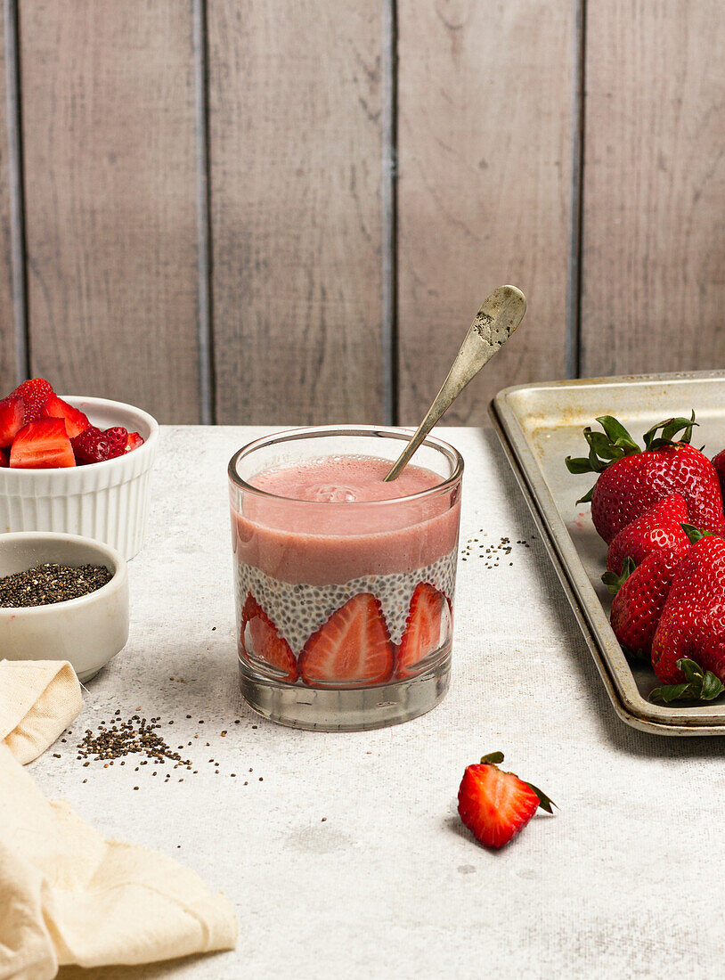 Leckerer Pudding mit Chiasamen und Scheiben von frischen Erdbeeren auf dem Tisch neben den Zutaten für ein gesundes Frühstück