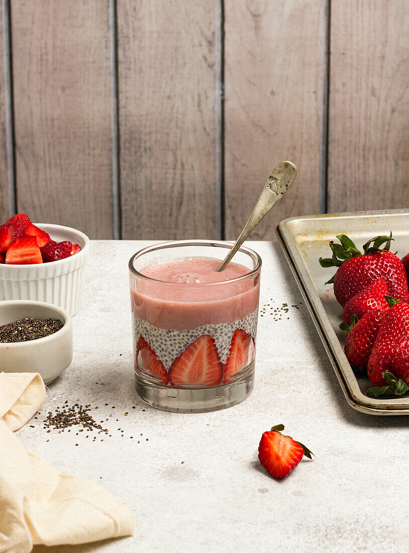 Tasty pudding with chia seeds and slices of fresh strawberries placed on table near ingredients for healthy breakfast