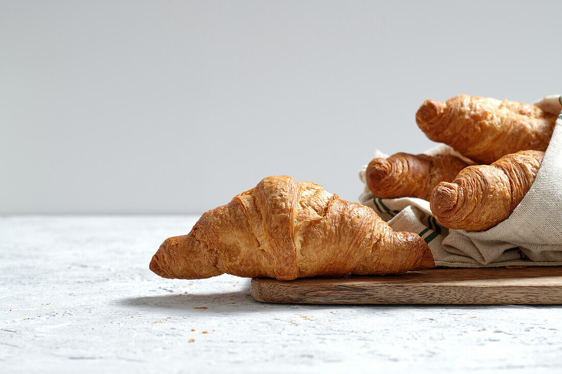 Frisch gebackene Croissants, serviert auf einem Holzbrett mit Serviette auf dem Frühstückstisch