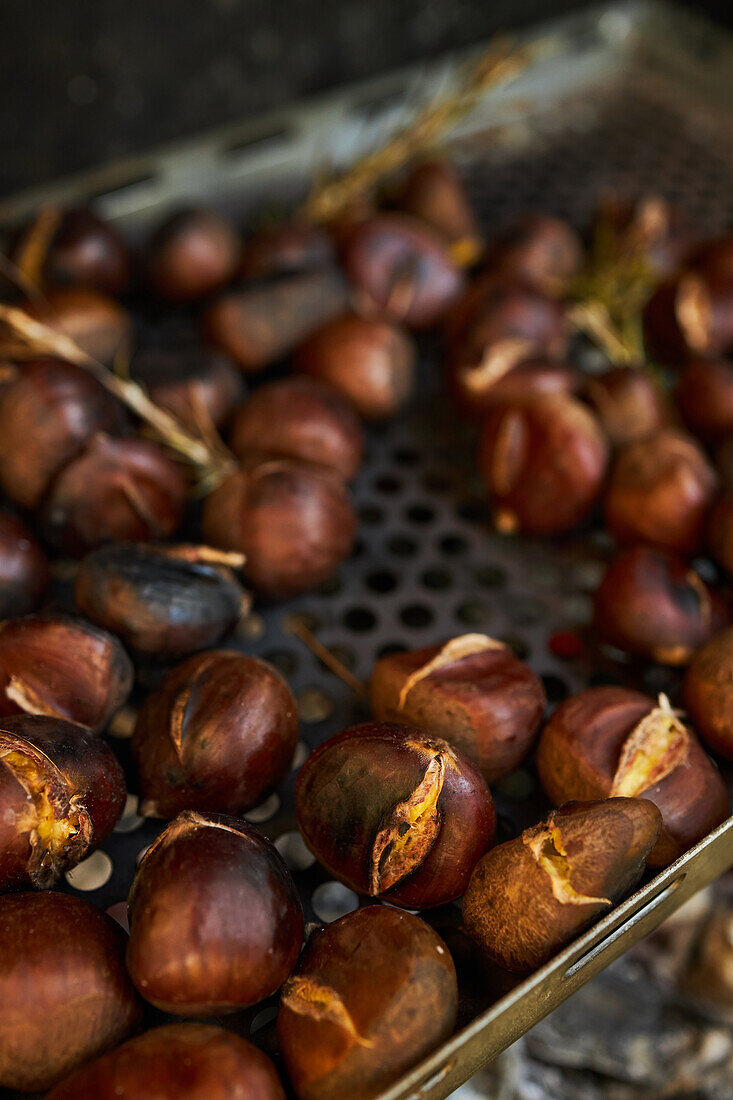 From above closeup of baked of pile of fresh chestnuts on metal tray near dry leaves on soil in autumn forest