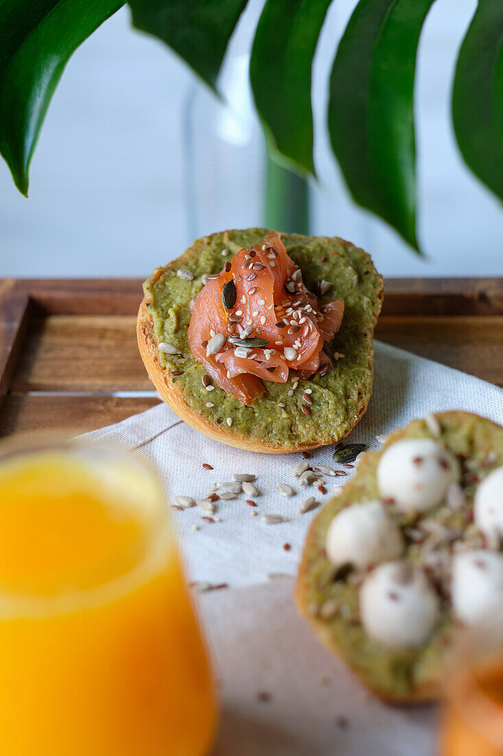 Gläser mit Saft und Kräutertee, serviert auf einem Holztisch mit verschiedenen gesunden Avocado-Toasts mit Käse und Lachs während des Frühstücks in einem Straßencafé