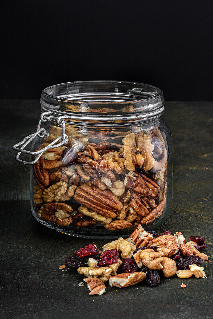 Glasgefäß mit Nüssen und Trockenfrüchten vor dunklem, rustikalem Hintergrund