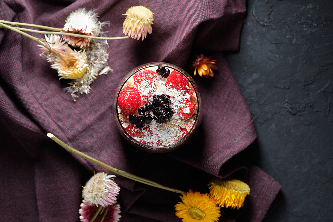 Appetitanregende Smoothie-Schale mit Granola, Erdbeeren und Blaubeeren auf einem Tisch in der Nähe verschiedener Wildblumen