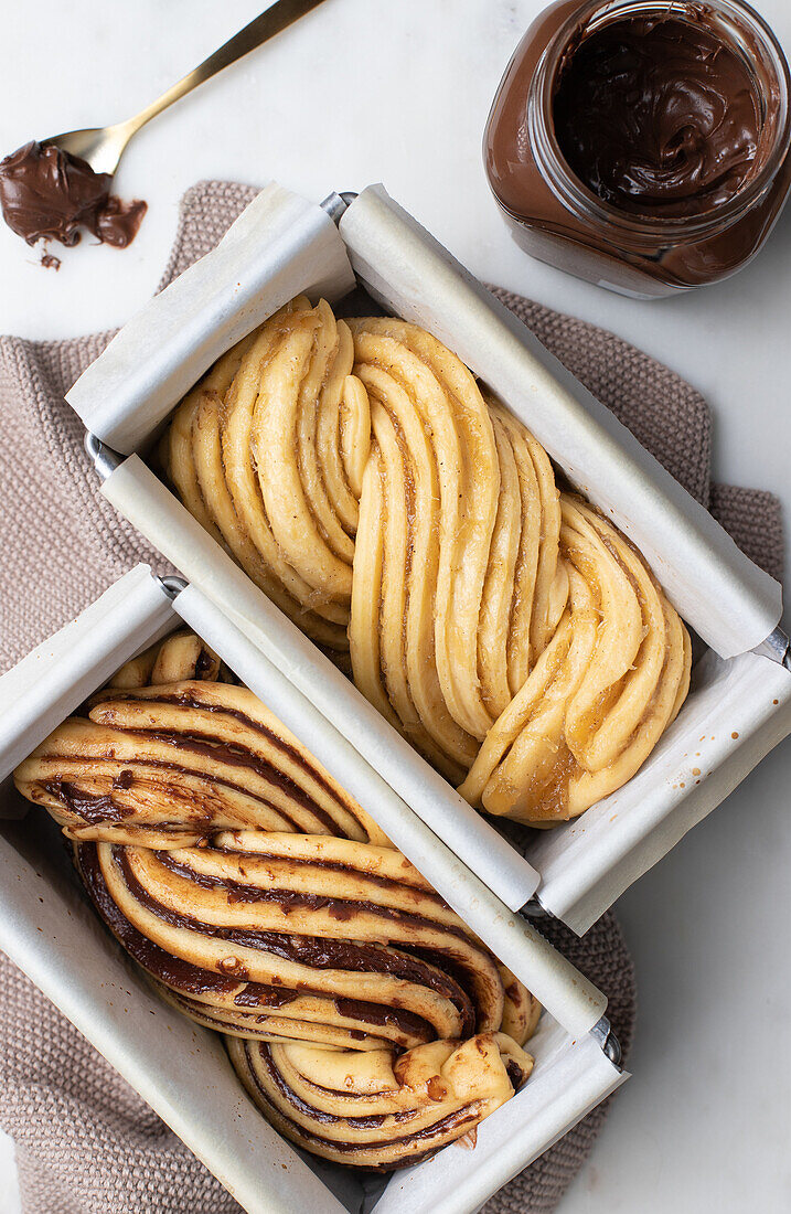 Uncooked Babka cake with chocolate paste placed on baking paper in metal dish in kitchen