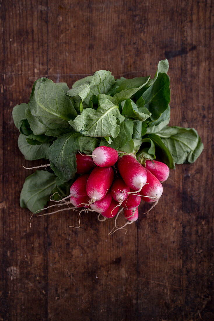 Top view of heap of raw radish with curved leaves and roots on brown background