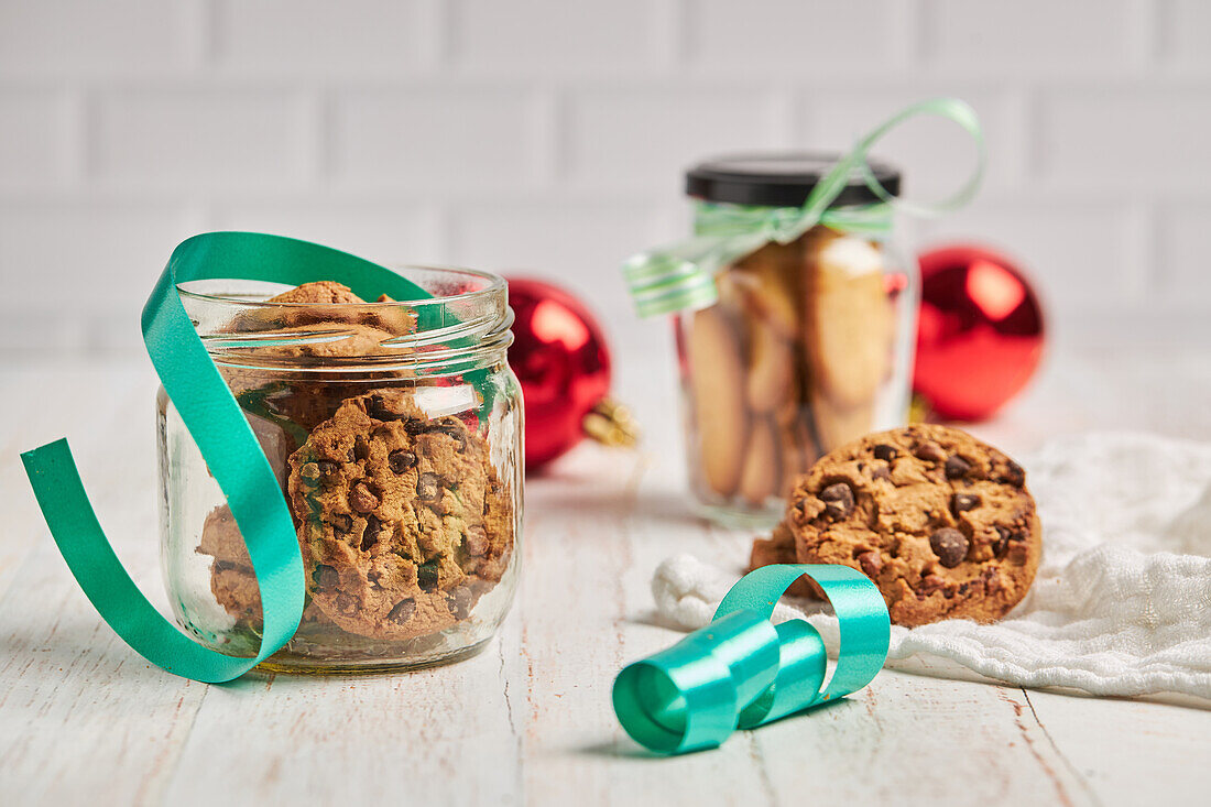 Homemade chocolate chip Christmas biscuits in glass jars placed on table with ribbons and baubles