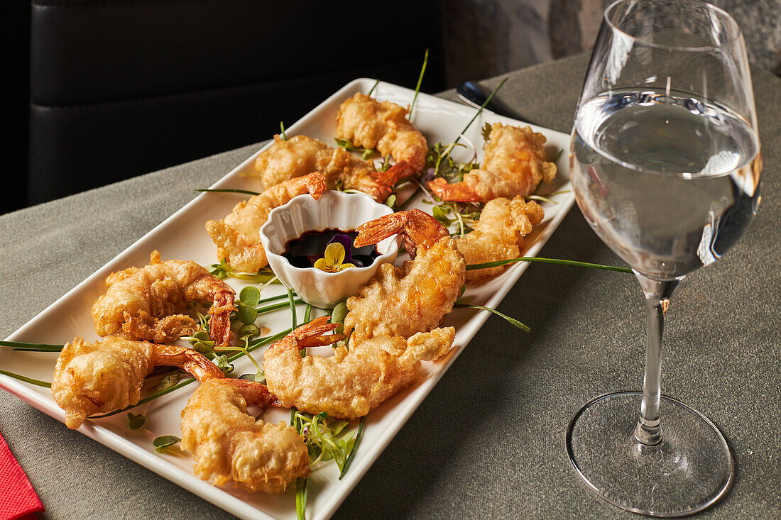 From above tasty shrimp tempura with greens and soy sauce served on plate near glass of water on restaurant table