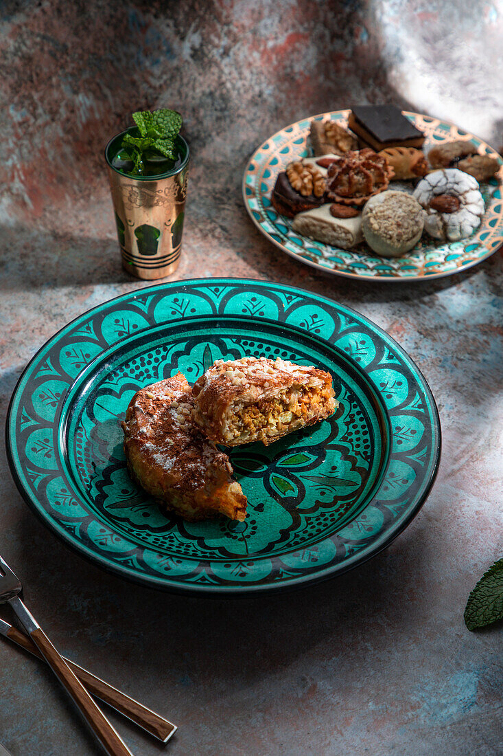 Von oben Baklava und Kekse mit marokkanischem Pfefferminztee neben Messer und Gabel auf einem mit Minzblättern dekorierten Tisch