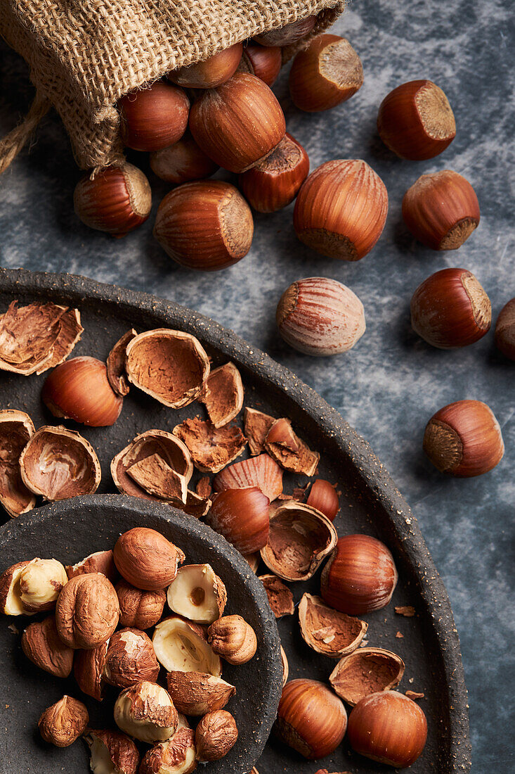 From above bunch of ripe hazelnuts and shells scattered on plate and marble table near burlap bag