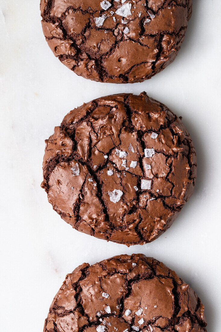 Draufsicht auf süße, frisch gebackene Schokoladen-Brownie-Kekse mit Rissen auf weißem Hintergrund in einer hellen Küche zu Hause