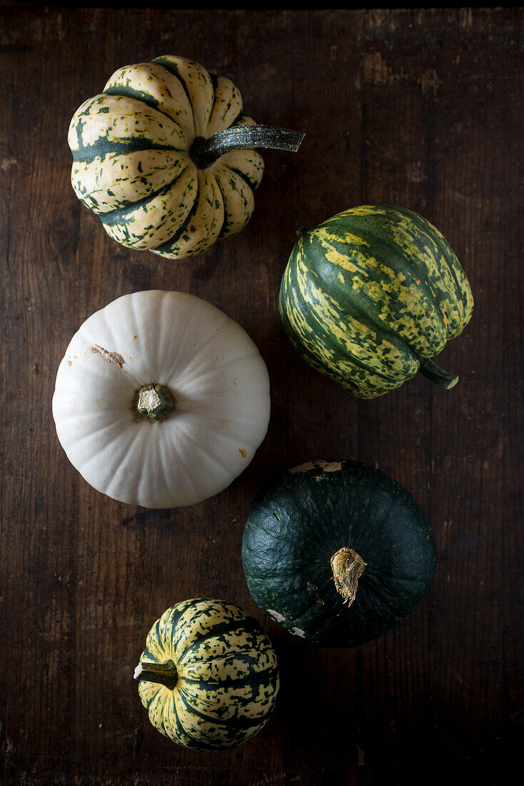 From above whole fresh decorative pumpkins with striped peel on dark wooden table background