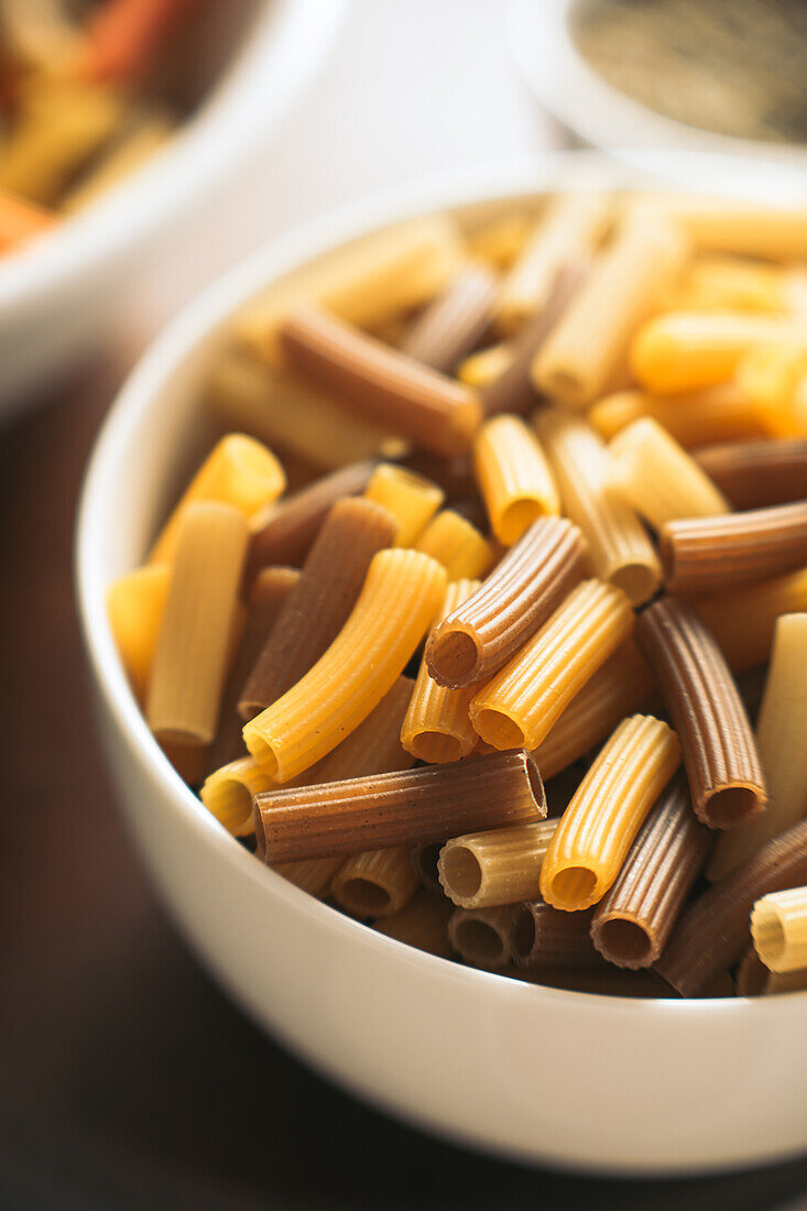 Closeup white ceramic bowl filled with dark and pale uncooked pasta