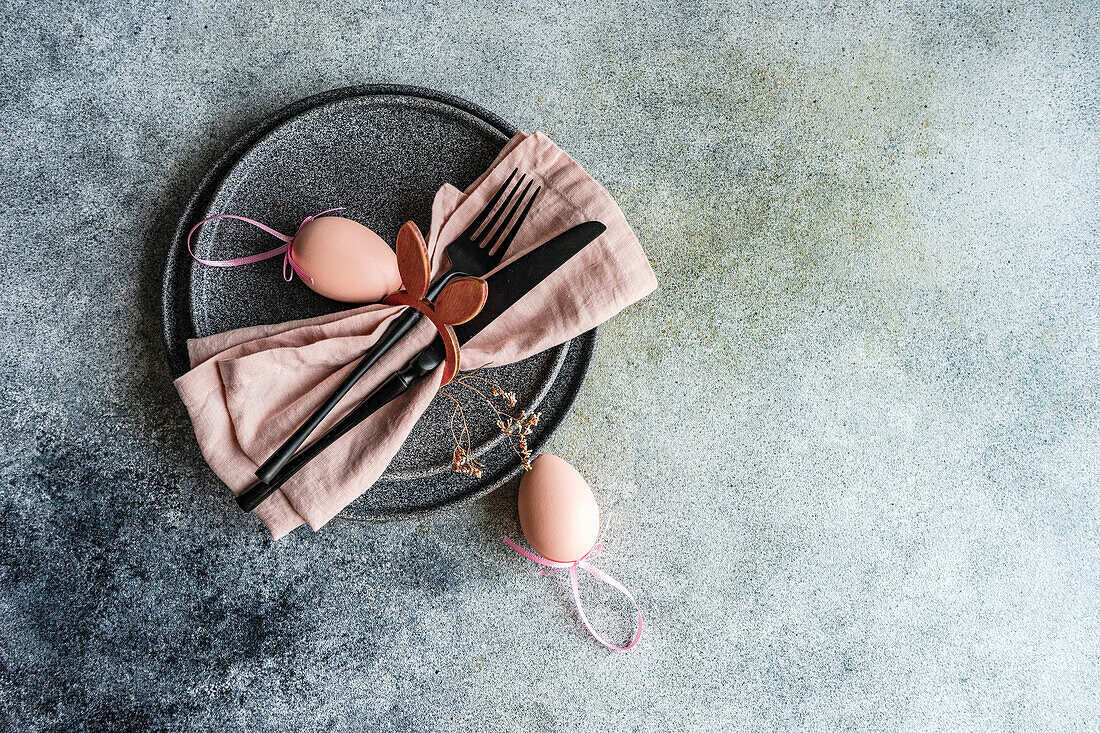 From above table set for Easter dinner with pink napkin and eggs on concrete background