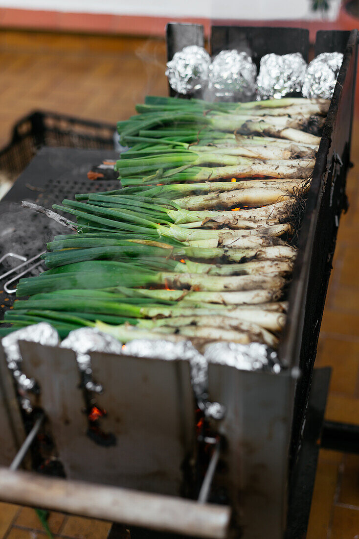 Heap of traditional Catalonian fresh green calcots on black metal hot grill with foil and burning charcoal placed on terrace