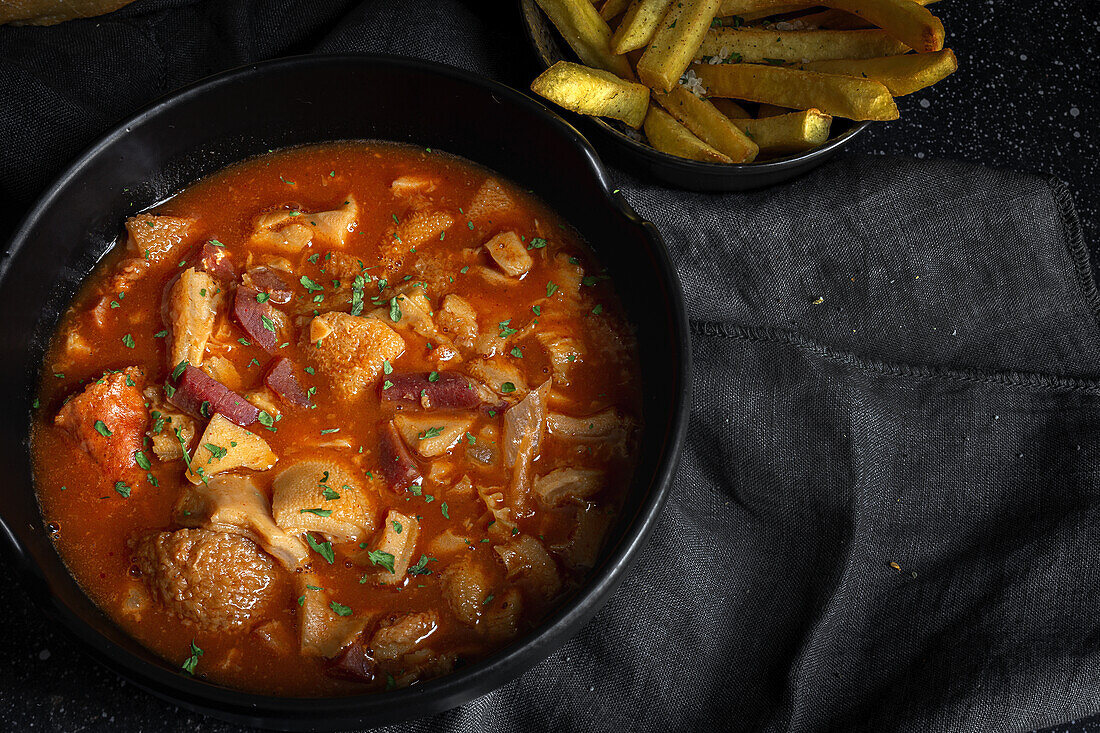 From above of tasty callos a la madrilena in black bowl near French fries on table