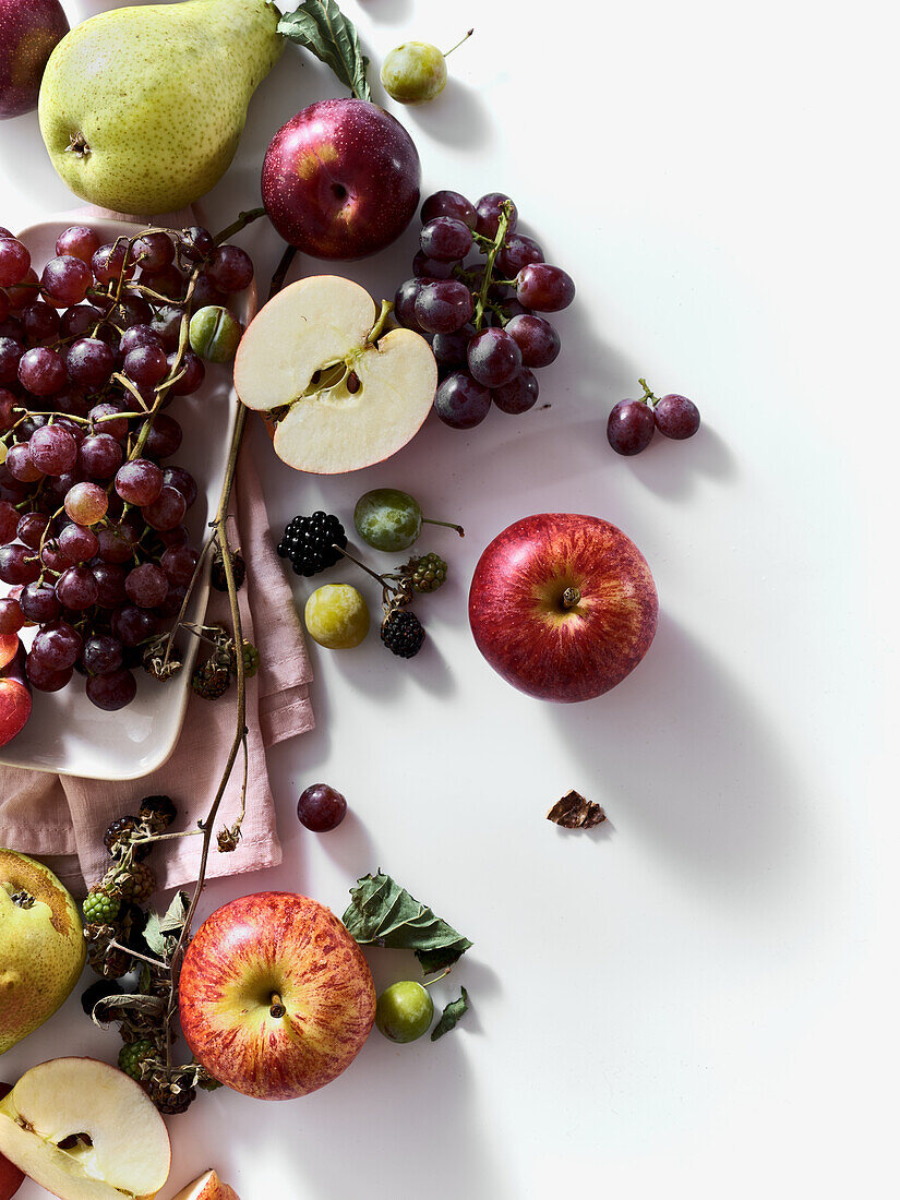 Composition with fresh summer fruits and berries on white background. Grapes, plums and apples in sunlight.
